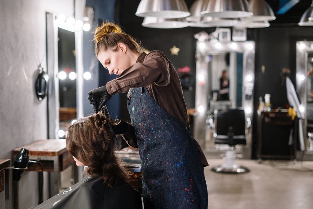 A hairdresser in gloves colouring a client’s hair