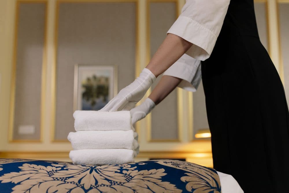 A housekeeper stacking fresh towels on a hotel bed